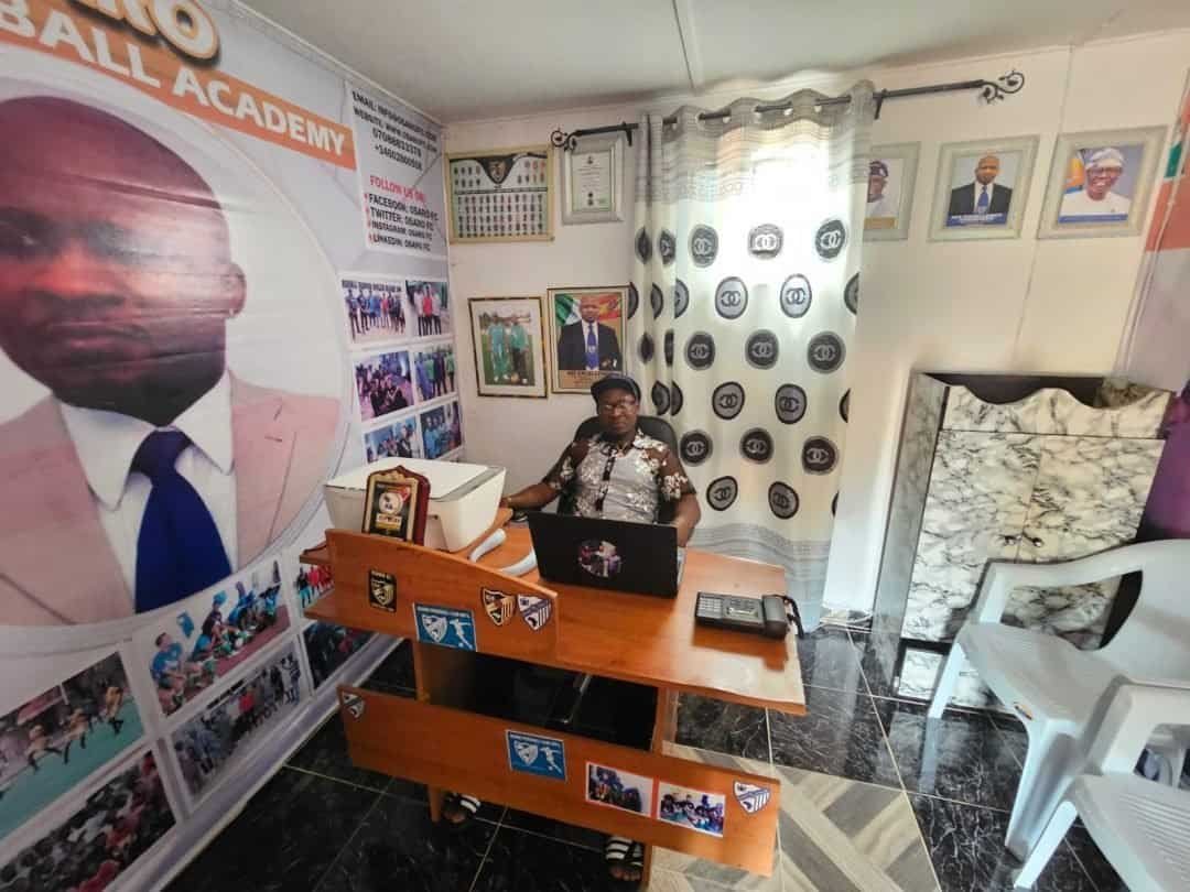 OFF Young woman at Osaro Intl Sports Academy office, surrounded by sports memorabilia and motivational posters.