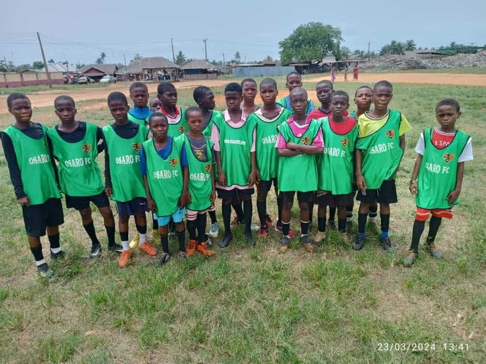 Grass field with young Osaro FC soccer players in green jerseys, practicing football skills at Osaro International Sports Academy, focused on youth sports development.