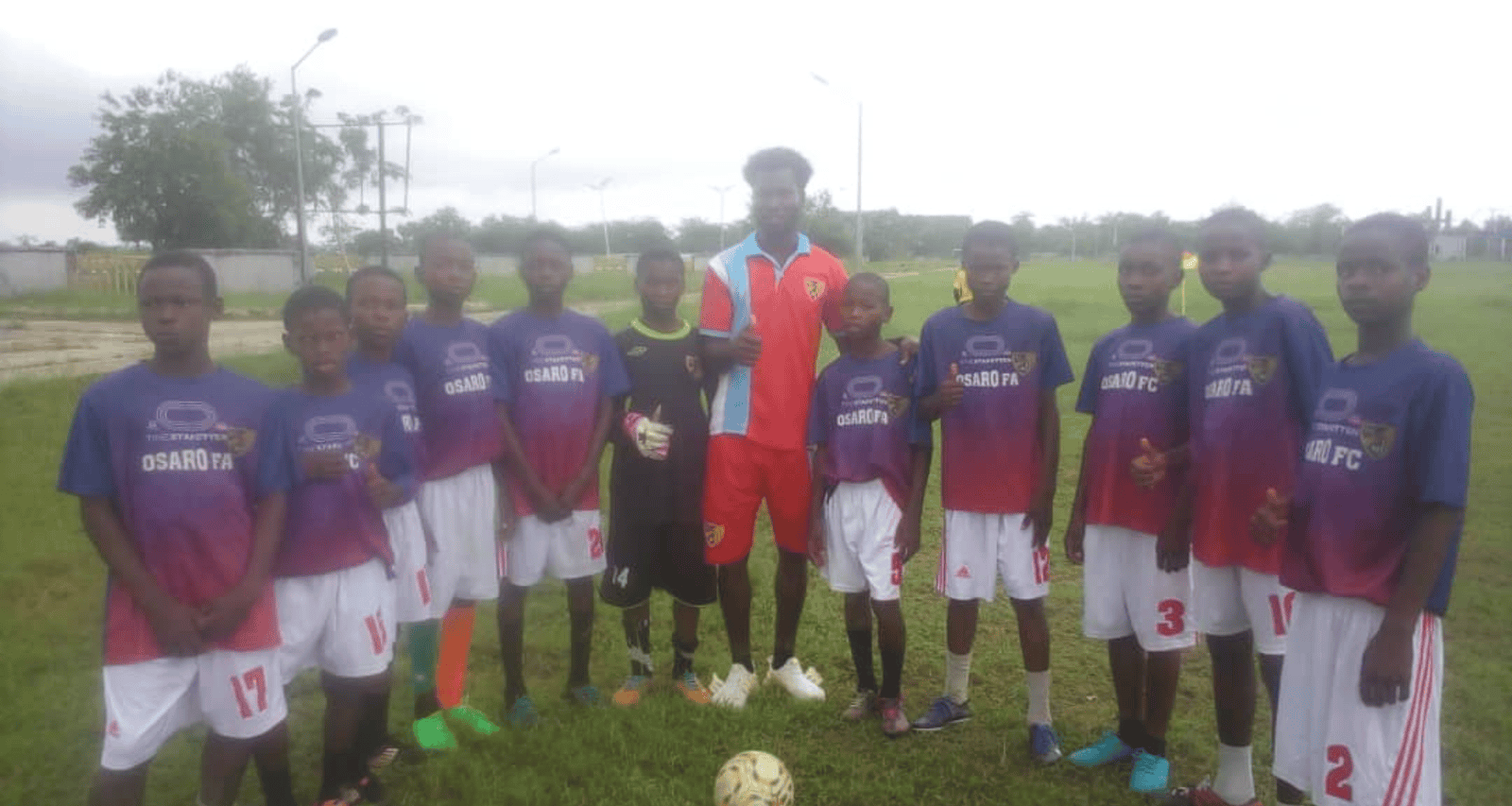 Young soccer players at Osaro Intl Sports Academy team photo with coaches on the field.